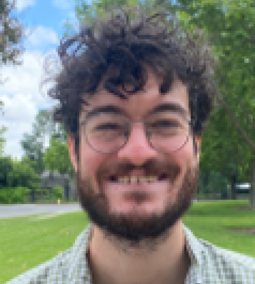 Smiling young man with curly hair, glasses and beard, outdoor portrait in park