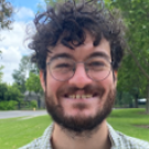 Smiling young man with curly hair, glasses and beard, outdoor portrait in park