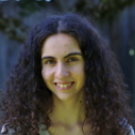Smiling woman with curly dark hair outdoors, close-up portrait photograph