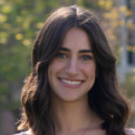 Smiling young woman with dark wavy hair, outdoor headshot photo, blurred green background